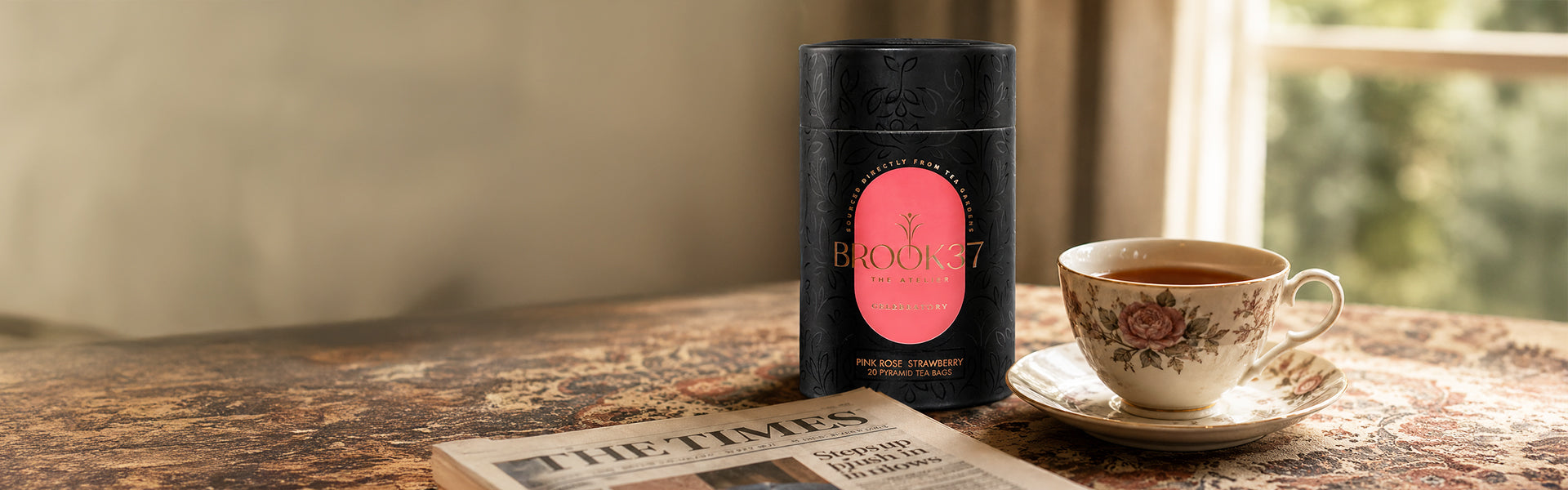 Black cylindrical coffee canister with pink label on a wooden table with a cup of coffee and newspaper.