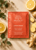 Brook37 Los Angeles Lemon Ginger green tea packet in a vibrant orange-red color, styled in a flat lay with fresh lemon slices, ginger root, and green leaves on a beige textured background.