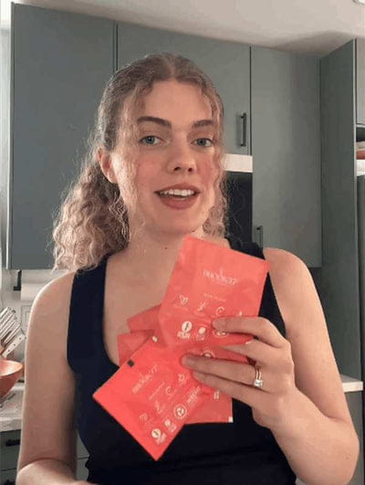 Woman holding three Brook37 tea sachets in a modern kitchen.
